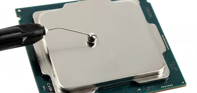 A syringe tip applying a small drop of liquid metal to the CPU's metal surface.